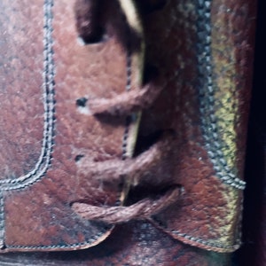 May include: Close-up of brown leather boots with laces tied in a knot. The laces are brown and the boots have a textured surface.