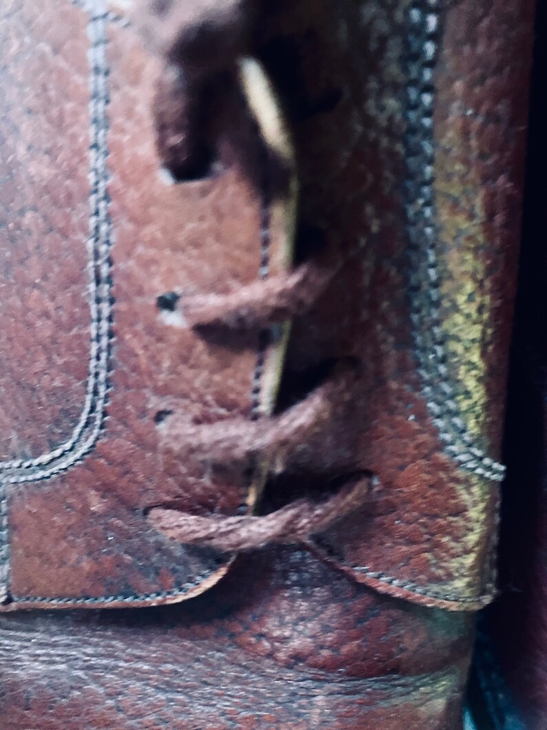 May include: Close-up of brown leather boots with laces tied in a knot. The laces are brown and the boots have a textured surface.