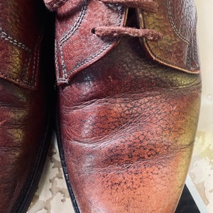 May include: Close-up of a pair of brown leather shoes with laces. The shoes have a worn and distressed look, with visible stitching and creases.