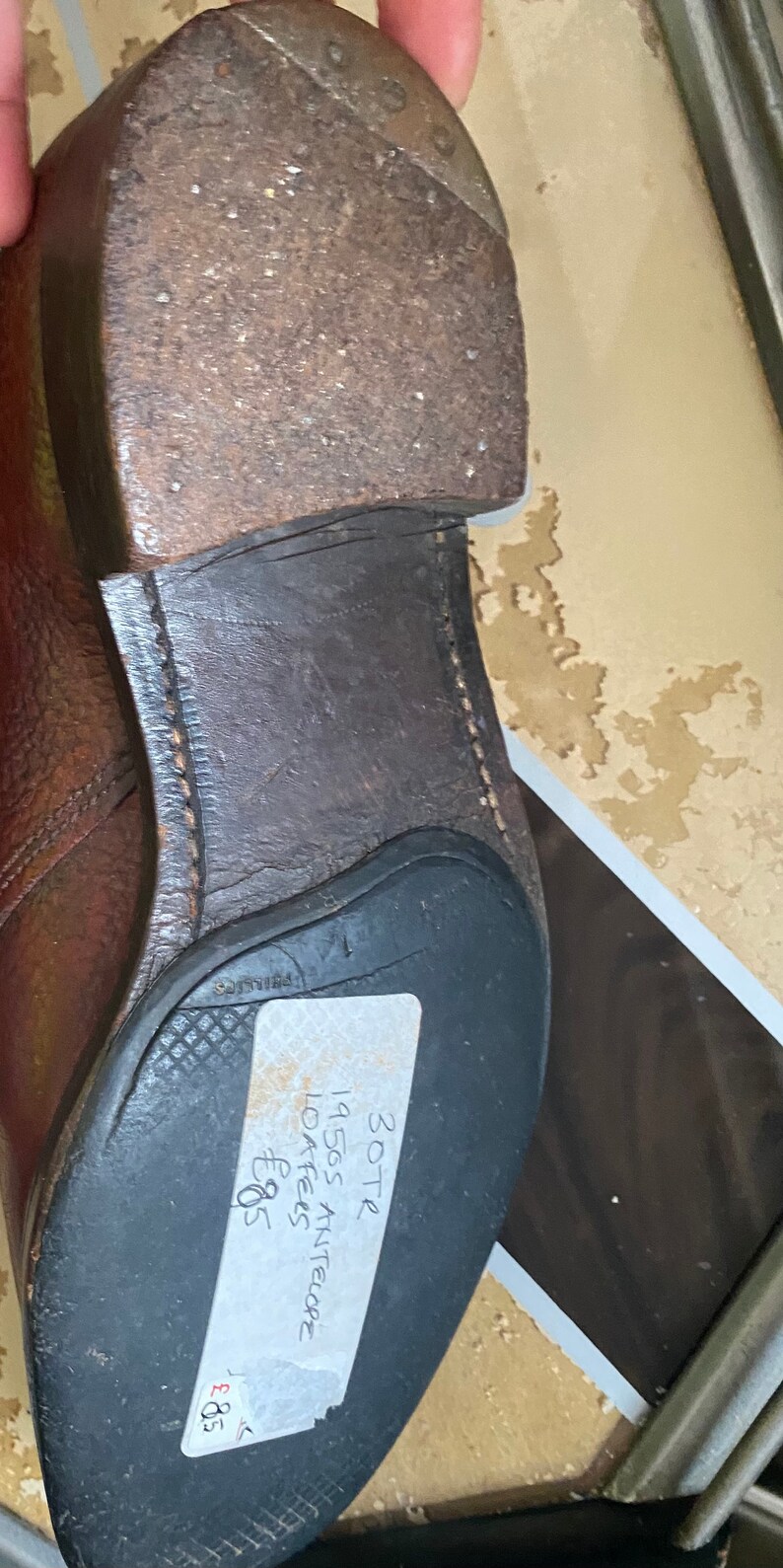 May include: A brown leather loafer with a black rubber sole. The shoe has a price tag attached to it that reads "30-TR 1950s Antelope Loafers &pound;8.95".