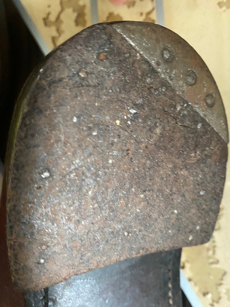 May include: Close-up of a worn leather shoe sole with a metal heel plate. The sole is brown and has a rough texture. The heel plate is silver and has a few small holes.