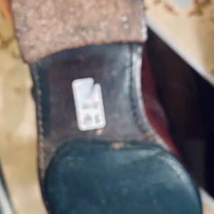 May include: Close-up of the bottom of a brown leather boot with a black rubber sole. The boot has a worn leather upper and a stitched seam around the sole.