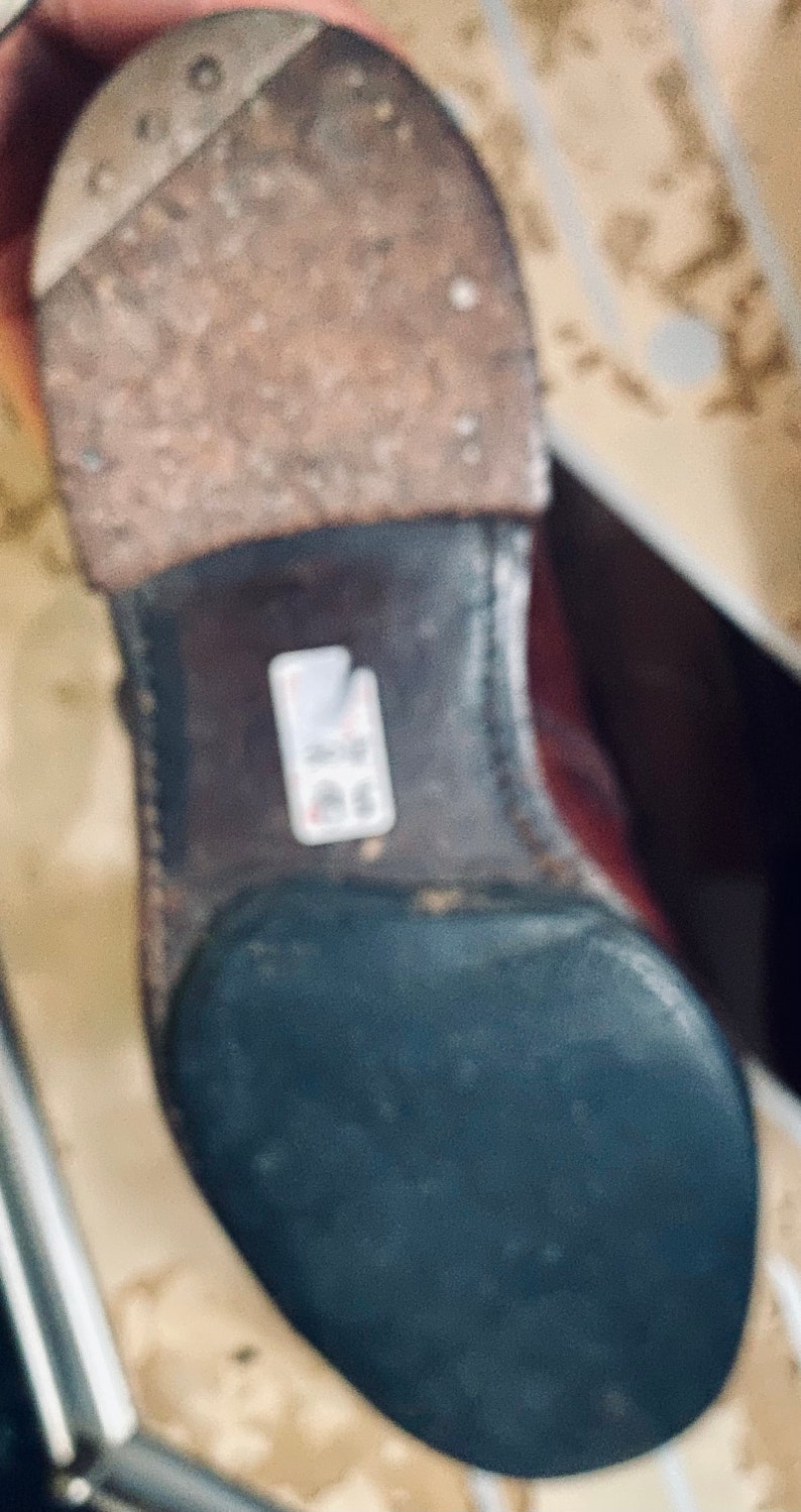 May include: Close-up of the bottom of a brown leather boot with a black rubber sole. The boot has a worn leather upper and a stitched seam around the sole.