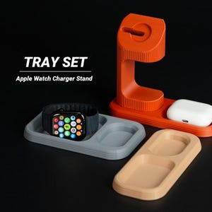 Peut inclure: Un support de chargeur Apple Watch orange avec un plateau pour AirPods et deux plateaux supplémentaires gris et beige. Le texte "TRAY SET" et "Apple Watch Charger Stand" sont affichés en blanc.