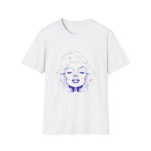 Puede incluir: Camiseta blanca con una ilustración azul y morada del rostro de una mujer. El gráfico, centrado en la parte delantera, representa a una mujer con los ojos cerrados y el pelo ondulado. La camiseta tiene mangas cortas y cuello redondo.