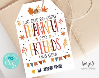 Puede incluir: Una etiqueta de regalo de Acción de Gracias con un tema otoñal. La etiqueta es blanca con hojas naranjas, amarillas y marrones y una pancarta con el texto "We are so very thankful for friends like you!" La etiqueta también incluye el texto "The Johnson Family" y un pequeño corazón.