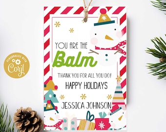 Pode incluir: Uma etiqueta de presente branca com listras vermelhas e brancas. Apresenta um boneco de neve com um chapéu verde e uma echarpe vermelha. O texto diz "You are the Balm. Thank you for all you do! Happy Holidays Jessica Johnson".