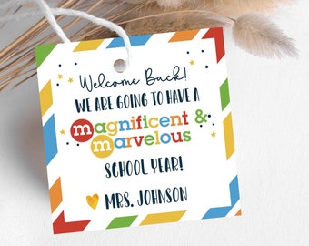 Puede incluir: Una etiqueta blanca con un borde colorido y el texto "Welcome Back! We are going to have a magnificent & marvelous SCHOOL YEAR! MRS. JOHNSON." La etiqueta tiene una cuerda para colgar.