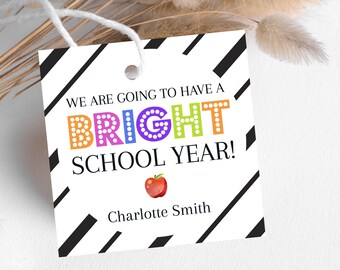 Op de afbeelding: Witte cadeaukaart met zwarte diagonale strepen. De kaart heeft de tekst "We are going to have a BRIGHT SCHOOL YEAR!" met het woord "BRIGHT" in kleurrijke letters met witte stippen. Onder de tekst staat een rode appel-emoji. De kaart is gepersonaliseerd met de naam "Charlotte Smith".