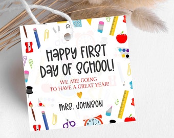 Op de afbeelding: Een wit cadeau-etiket met een kleurrijk patroon van schoolbenodigdheden. De tekst luidt "Happy First Day of School! We are going to have a great year! Mrs. Johnson".