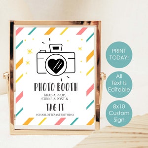 Puede incluir: Un cartel de cabina de fotos imprimible de 8x10 pulgadas con un fondo a rayas de colores y un icono de cámara en blanco y negro. El texto dice "Photo Booth Grab a Prop, Strike a Post & Tag It #Charlottes1stBirthday".
