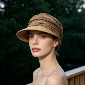 May include: A woman wearing a brown sun hat with a brim. The hat has a textured crown and a lighter-colored brim. The background is a blurred view of green trees.