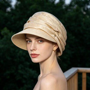 May include: A beige sun hat with a wide brim and a gathered crown. The hat has a structured design with a slight sheen. The hat is made of a woven material and is suitable for sun protection. The hat is a stylish accessory.