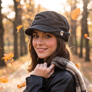 Peut inclure: Une casquette gavroche gris anthracite foncé dotée d'une calotte en tissu souple et froncé ainsi que d'une visière courte et incurvée. La casquette est ornée d'un bouton unique, lisse et argenté sur le côté, contrastant avec la matière texturée.