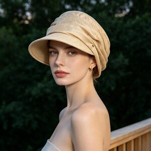 May include: A beige sun hat with a rounded crown and a short brim. The hat is made of a textured fabric and has a decorative element on the side. The hat is worn by a person with fair skin and light eyes.