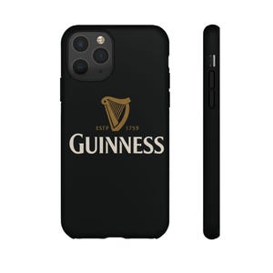 Puede incluir: Funda de teléfono negra con el logotipo de Guinness. El logotipo incluye un arpa dorada y la palabra "GUINNESS" en blanco, con "ESTP 1759" encima del logotipo. La funda se muestra de frente y de lado.