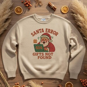 May include: Beige crewneck sweatshirt with a Christmas-themed graphic. The graphic features Santa Claus with a laptop displaying "404" and the text "SANTA ERROR GIFTS NOT FOUND" in red and green. The sweatshirt is surrounded by dried orange slices and cinnamon sticks.