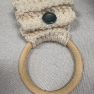 Peut inclure: Porte-serviette en crochet crème avec un anneau en bois. Le support est orné d'un bouton décoratif et d'un motif texturé. L'anneau en bois est de couleur brun clair. Le crochet a un léger scintillement.