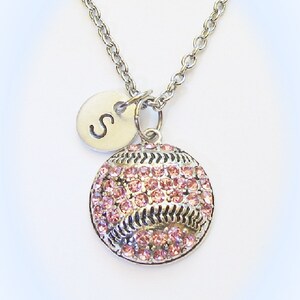 May include: A silver chain necklace with a pink rhinestone softball charm and a silver charm with the letter "S" on it.