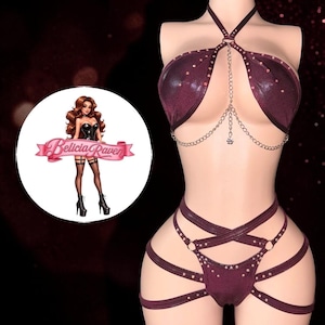 May include: A dark maroon metallic two-piece lingerie set featuring a halter-style top with silver chain accents and studs, paired with strappy high-cut bottoms. A circular logo graphic displays a cartoon character and the text Belicia Raven.