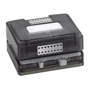 May include: A black, rectangular paper punch with a clear top and silver accents. The punch has a rectangular opening and a silver metal base. The top has a decorative silver pattern.