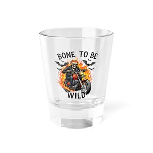 May include: A clear shot glass with a graphic of a skeleton riding a motorcycle engulfed in flames. The text "BONE TO BE WILD" is above and below the image, with bats in the background.