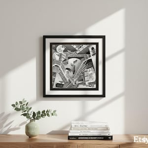 Puede incluir: Impresión enmarcada en negro de la obra "Relatividad" de M.C. Escher. La litografía en blanco y negro representa una compleja estructura arquitectónica con escaleras y figuras interconectadas. La impresión se exhibe en una pared blanca.