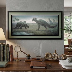Puede incluir: Una impresión artística enmarcada de dinosaurios, con un Tyrannosaurus Rex y un Triceratops en un paisaje prehistórico. La obra de arte está en un marco negro con un borde verde. La escena incluye una masa de agua y un campo cubierto de hierba. La impresión está sobre un escritorio de madera.
