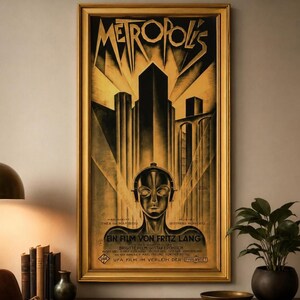 Puede incluir: Un póster de la película Metropolis enmarcado con un gráfico estilizado en negro y dorado de una cabeza de robot bajo un paisaje urbano imponente. El texto METROPOLIS aparece en la parte superior, con créditos de Fritz Lang y el reparto.