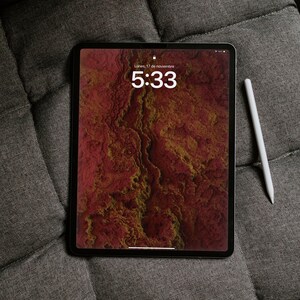 May include: A black tablet with a red and gold abstract background, displaying the time 5:33. A white stylus rests beside the tablet on a gray, textured surface. The date is displayed as Monday, November 17.