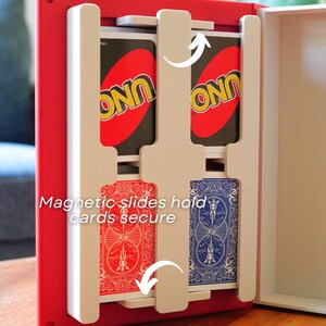 Op de afbeelding: Een rood-witte opbergdoos voor kaarten met witte magnetische schuiven die kaartspellen veilig op hun plek houden. De binnenkant toont twee UNO-kaartspellen bovenaan en twee standaard speelkaartspellen met rode en blauwe achterkanten onderaan.