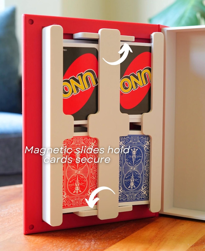 Op de afbeelding: Een rood-witte opbergdoos voor kaarten met witte magnetische schuiven die kaartspellen veilig op hun plek houden. De binnenkant toont twee UNO-kaartspellen bovenaan en twee standaard speelkaartspellen met rode en blauwe achterkanten onderaan.