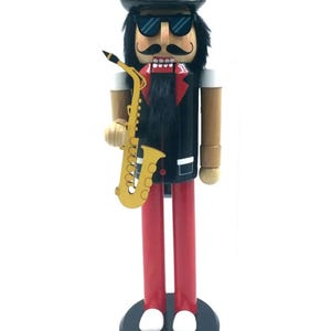 Puede incluir: Una taza de cerámica blanca con un asa negra y el texto "But First, Coffee" en negrita negra. La taza se encuentra sobre un fondo borroso, sugiriendo un ambiente acogedor.