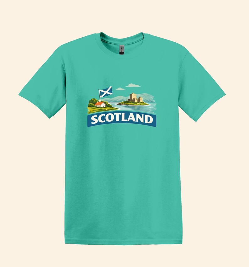 May include: Teal t-shirt featuring a graphic of a Scottish landscape with a castle, flag, and the word "SCOTLAND" in white on a blue banner. The design includes a small house and rolling hills.