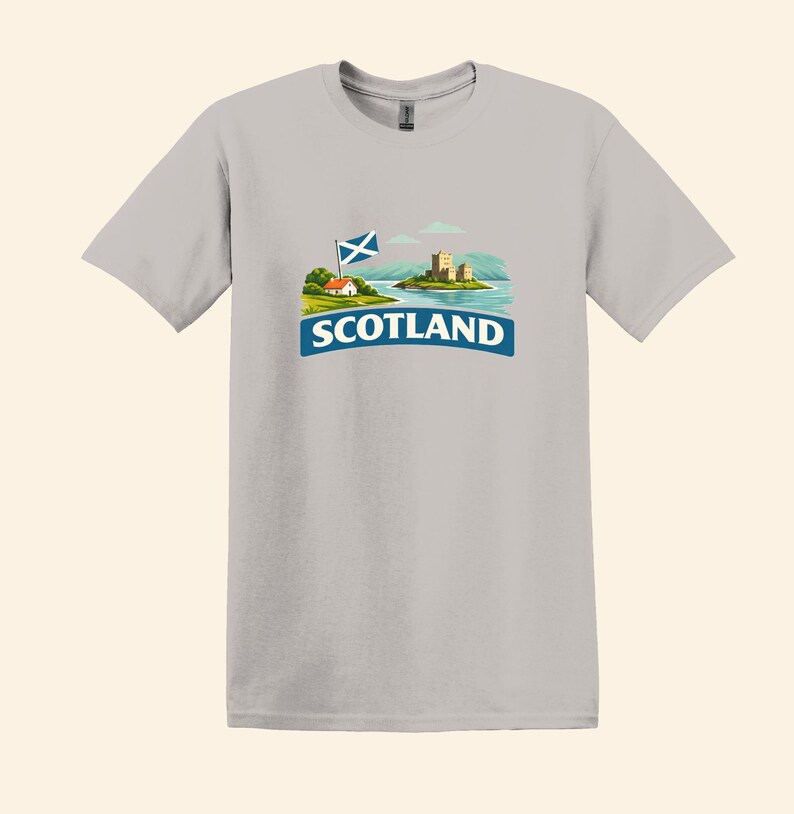 May include: A light gray t-shirt featuring a graphic of Scotland. The graphic includes a Scottish flag, a small house, a castle on an island, and the word "SCOTLAND" in a blue banner.