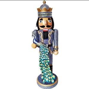 Puede incluir: Figura decorativa de cascanueces con un diseño regio. La figura viste un uniforme azul con detalles dorados y una corona. Sostiene un pavo real con una vibrante cola azul y verde. El cascanueces se encuentra sobre una base redonda.
