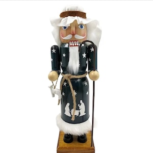 Peut inclure: Casse-noisette de Noël en bois en forme de berger, portant un chapeau et une barbe blancs. Le manteau bleu foncé est orné d'étoiles blanches et d'une scène de la Nativité. Le berger tient un bâton et un petit agneau.