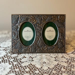 May include: A rectangular, antique pewter finish double photo frame. The frame features an embossed grape vine design around two oval openings with green backing. The text "PHILIP WAINWRIGHT LTD" is visible on the inserts. Each photo opening is 10 cm x 15 cm.