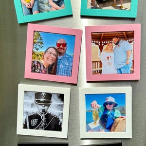 May include: Collection of framed photographs in various colors, including teal, pink, white, and black. The photos depict people, a cat, and a dog. The frames are square and appear to be magnetic.