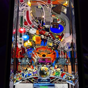 Könnte beinhalten: Ein Flipperautomat mit dem Thema "Addams Family". Das Spielfeld ist farbenfroh mit Rampen, Stoßstangen und Zielen. Das Display zeigt den Spielverlauf und das Addams Family Logo. Ein klassisches Arcade-Spiel.