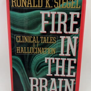 May include: A hardcover book titled Fire in the Brain: Clinical Tales of Hallucination by Ronald K. Siegel. The cover features a dark green marbled background with gold and white text, framed by a bold red border on the top and side edges.