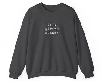 Puede incluir: Sudadera gris oscuro con el texto blanco "it's giving autumn". Esta sudadera de cuello redondo tiene mangas largas y un ajuste relajado, perfecta para el otoño. El diseño sencillo la convierte en una adición versátil a cualquier armario.