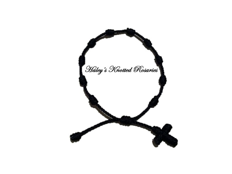 May include: A black knotted rosary bracelet with a small black cross charm. The bracelet is made of black cord and has a simple design. "Haley's Knotted Rosaries" is written in white text on a white background.