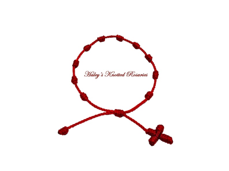 May include: Red knotted rosary bracelet with a cross charm. "Haley's Knotted Rosaries" is written on the bracelet.