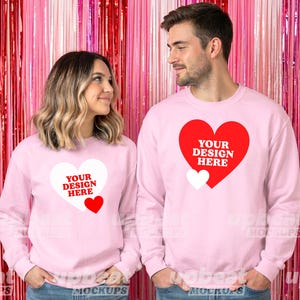 Puede incluir: Dos personas con sudaderas rosas a juego con un diseño de corazón. El diseño del corazón tiene el texto "YOUR DESIGN HERE" en blanco y rojo. El fondo es una cortina metálica rosa y roja.