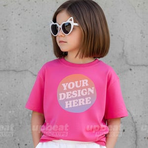 May include: A magenta t-shirt with a circular design that reads "YOUR DESIGN HERE" in white. The design has a gradient of orange, pink, and purple. The person is wearing cat-eye sunglasses.
