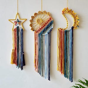 May include: Three handmade wall hangings: a star, a sun, and a crescent moon. Each piece features a woven design with colorful yarn tassels in shades of yellow, red, blue, and white. The star has a smaller star in the center.