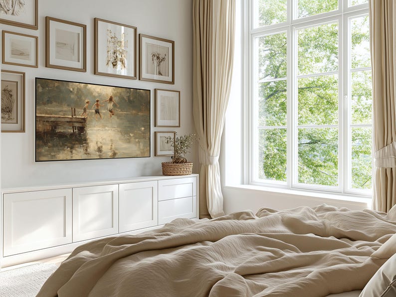 Puede incluir: Una habitaci&oacute;n con una gran ventana y cortinas beige. Una pintura de ni&ntilde;os saltando al agua cuelga sobre un mueble blanco. Varias obras de arte enmarcadas est&aacute;n dispuestas en la pared. Una cama con ropa de cama beige est&aacute; en primer plano.