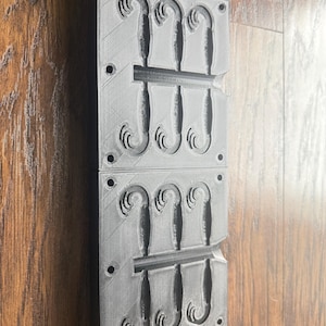 May include: Two gray, rectangular molds stacked on top of each other. Each mold has a series of curved, decorative shapes. The molds are made of a textured material and have several small holes along the edges.