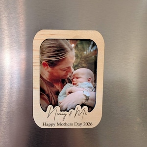 Puede incluir: Imán para fotos de madera con una foto de una persona sosteniendo a un bebé. El imán tiene las palabras "Nanny & Me" y "Happy Mothers Day 2026" grabadas. El imán es rectangular con esquinas redondeadas.